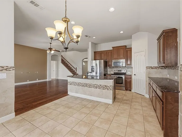 Kitchen featuring wood finish cabinetry, stainless steel appliances, vaulted ceiling, dark stone counters, and hanging lights