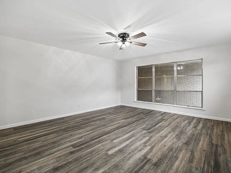 Spacious interior room featuring wood-finish flooring, white walls, and a large window with white brick exterior