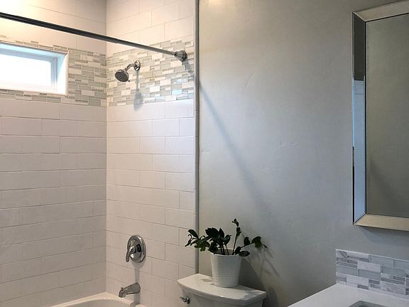 Large bath with tub/shower combination, white subway tiles, grey vanity cabinetry, quartz counter, marble/glass accents, tile floors, lighting, 9 foot ceilings