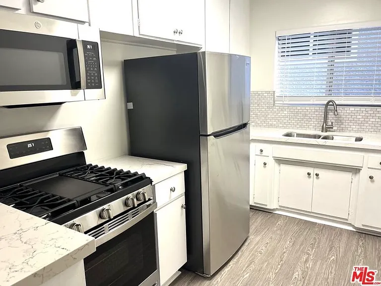 View of kitchen with stove, microwave, refrigerator, cabinetry, sink.