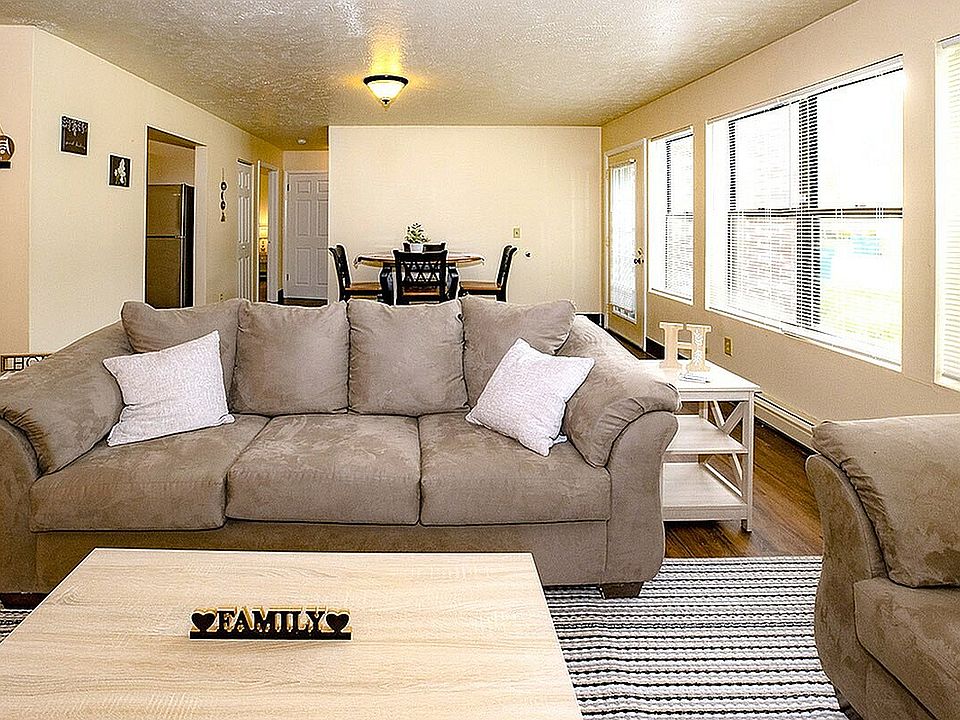 Inviting living room with plush beige couches, a cozy dining area, and abundant natural light through large windows.