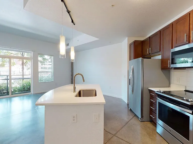Apartment kitchen with stainless steel appliances, dining and living room with polished concrete flooring.itchen with an island counter