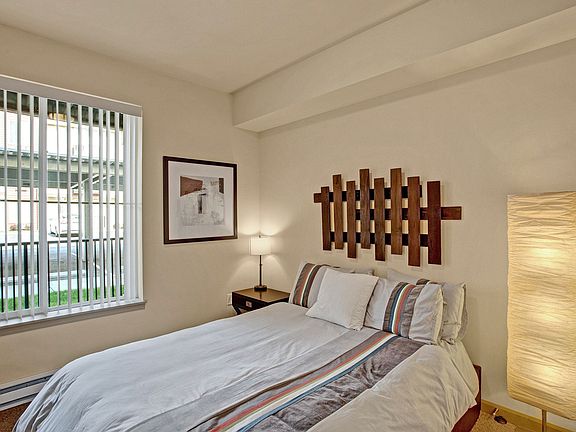 A bedroom with a bed and nightstand with a large window looking out to the property