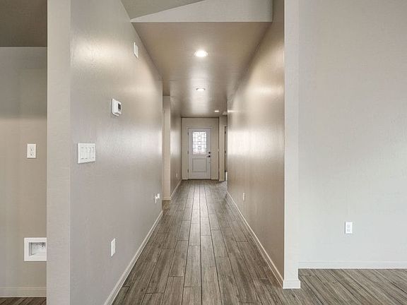A long, narrow hallway with light beige walls and wood-look tile flooring, leading to a white door w