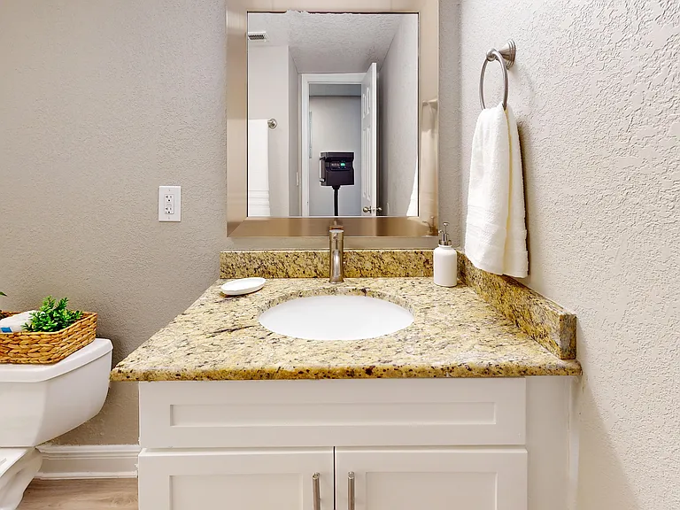Elegant bathroom showcasing a granite countertop with modern faucet, towel holder, and a decorative basket on the toilet.