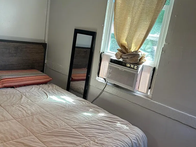 Private bedroom with a bed, window A/C unit, and a sunlit windowideal for comfortable day-to-day living.