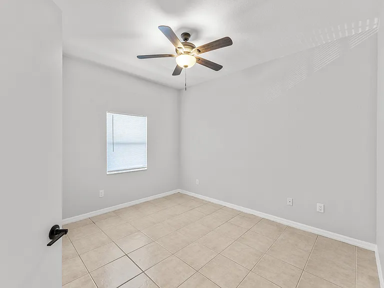 Bright, empty room with elegant tiled flooring, modern ceiling fan, and soft natural lighting through a window.