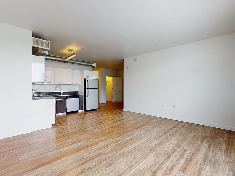 Apartment kitchen with stainless steel appliances, dining and living room with wood-style or concrete flooring.