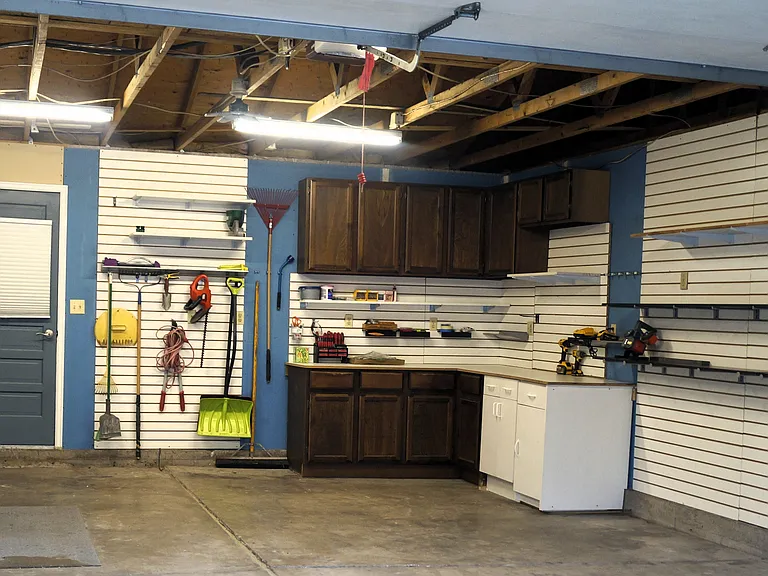 Well-lit oversized 24.5' X 19.5" 2-car garage with storage cabinets and slat board walls with adjustable shelves.