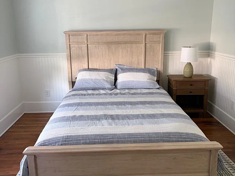 Furnished bedroom with a full bed, nightstand and lamp, hardwood floors, wainscoting, and mini-split A/C.