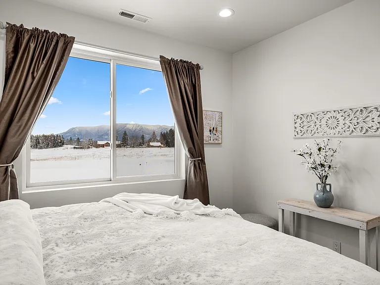 Peaceful suite framed by breathtaking mountain views, with a king-size bed shown for staging purposes only, creating a warm and restful Montana retreat.