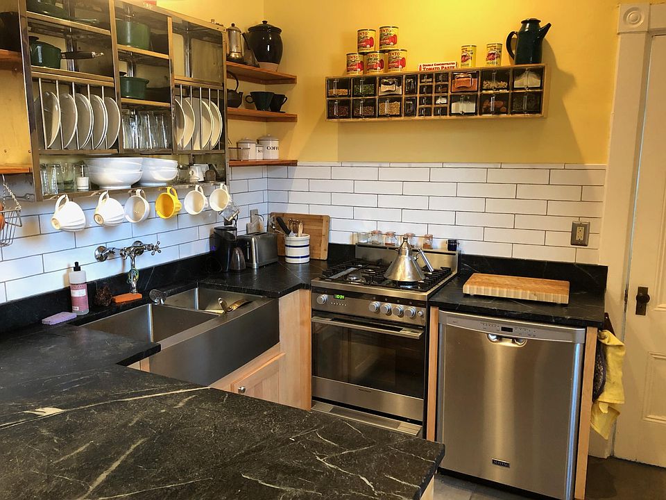 Kitchen with stainless steel sink, Fisher & Paykel gas range and electric convection one, soapstone countertops, and open shelves.