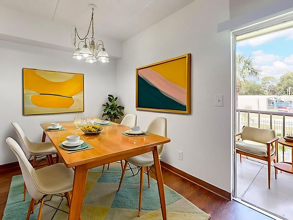 Bright and inviting dining area with modern decor, featuring a wooden table set for four, vibrant abstract artwork, and a petite balcony view.