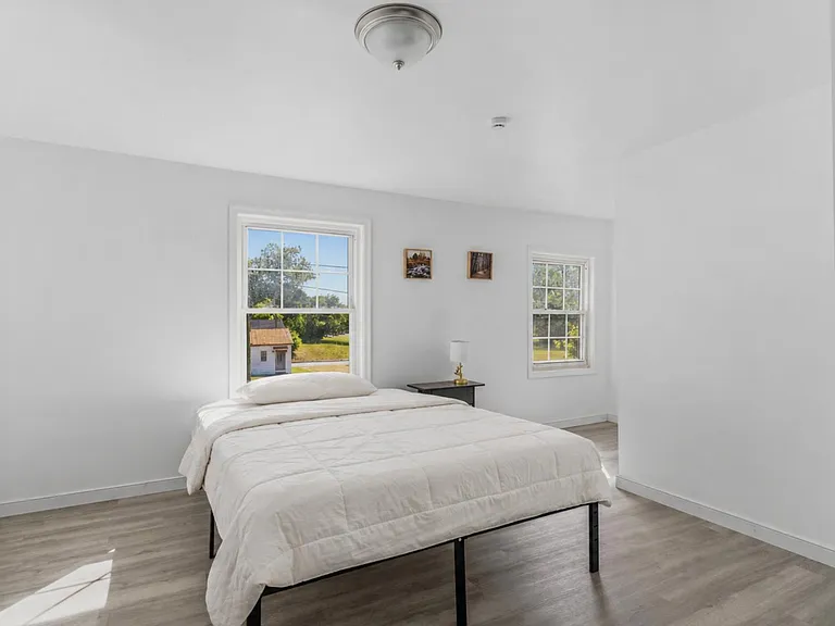 Spacious bedroom with two windows, wood-look flooring, and room for a full/queen bed plus a nightstand.