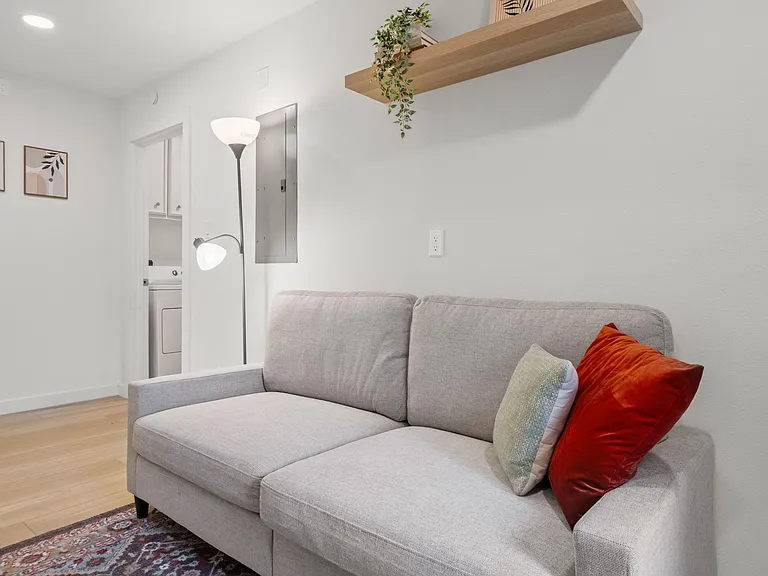 Inviting living area with a comfortable sofa, floating shelf, and easy access to nearby laundry for everyday convenience.