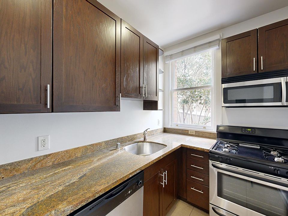 A modern kitchen with wood cabinets, countertops, a stainless steel stove and microwave, and a window bringing in natural light.