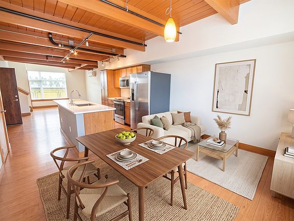 Open-concept floor plan at Union Bay Lofts in Seattle featuring exposed wood beams, stainless steel kitchen appliances, and dedicated dining space.
