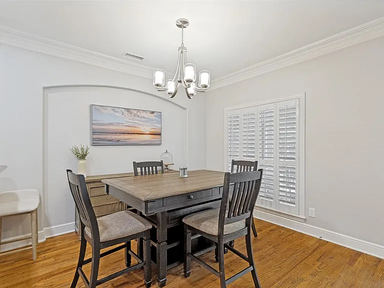 Dining area featuring wood-finish flooring, white plantation shutters, a recessed wall niche, and crown molding