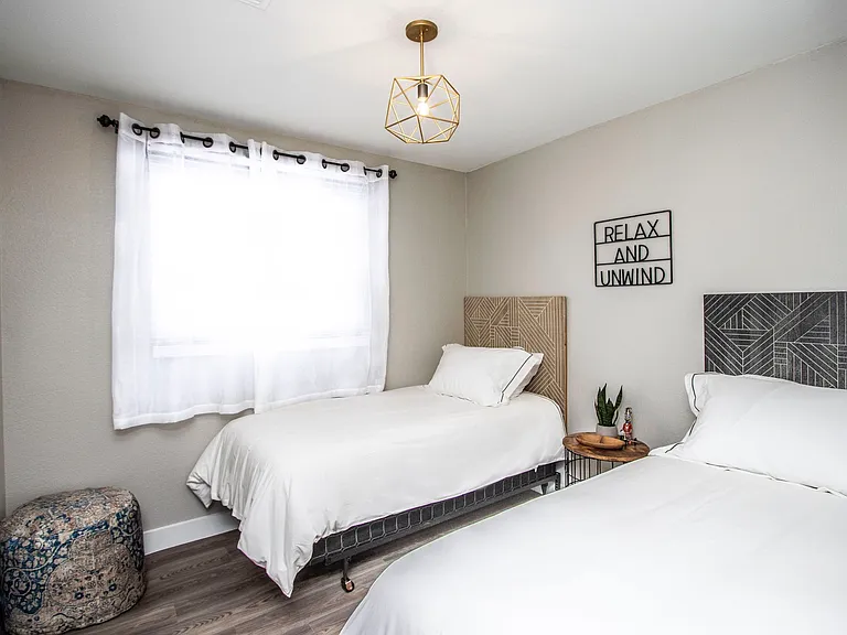Charming twin bedroom at Casa Del Sol, Tempe rental home. Features two twin beds with unique geometric headboards, gold pendant lighting, "Relax and Unwind" wall art, and a patterned pouf. Ideal for family, traveling nurses or group stays in Tempe, AZ.