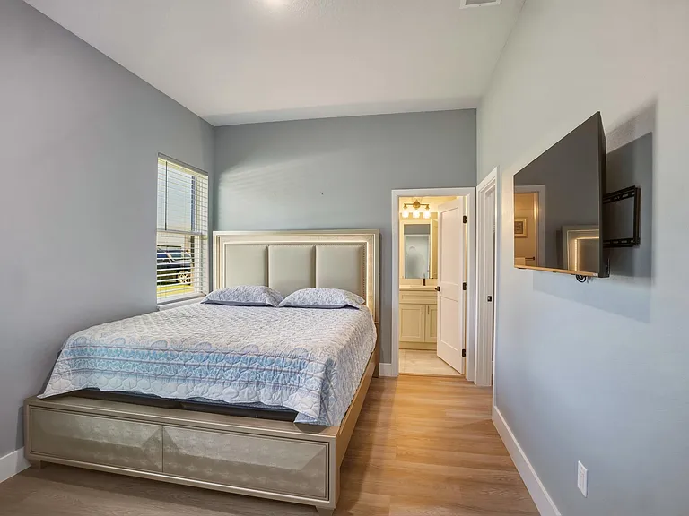 Bedroom features a queen bed, large window with blinds, wood-look flooring, and quick access to a nearby bathroom.