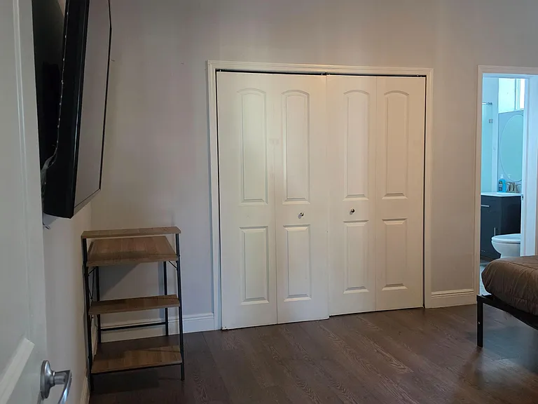 Bedroom with wood-look flooring, wall-mounted TV, and sliding-door closet, with convenient access to a nearby bathroom.