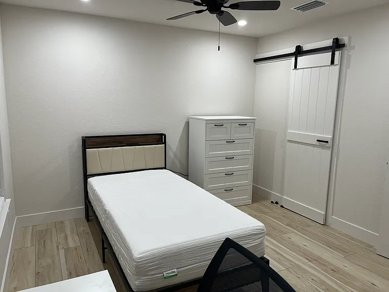 Furnished primary bedroom with TwinXL bed and mattress, tall dresser, desk, and chair.