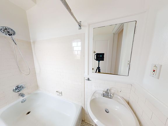 Bathroom featuring a shower, bathtub, and sink with tile walls and a mirror reflecting a camera on a tripod