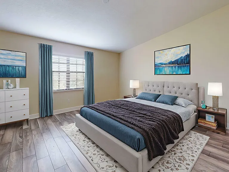 Elegant bedroom with a plush king-sized bed, soft blue and grey accents, large window with natural light, and tasteful artwork on the walls.