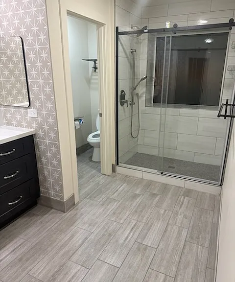 Large glass shower with diffused window baths the bathroom in natural lighting during the day. Separate toiled room with hotel-style towel storage area above toilet
