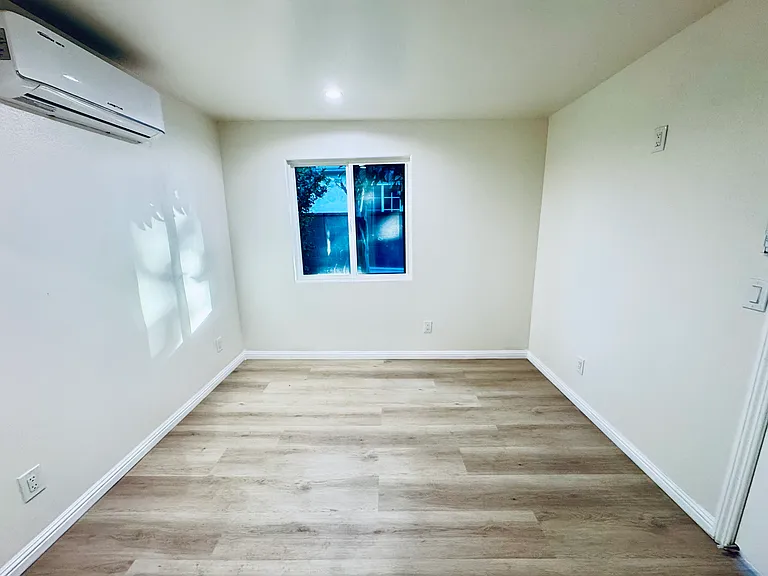 Spacious bedroom with window, AC unit, and sliding closet space.
