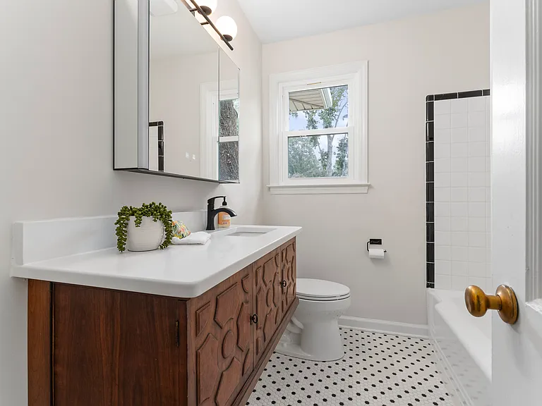 Renovated bathroom is the perfect mix of old and new with classic black and white tile, updated commode, illuminated medicine cabinet and floating vanity.