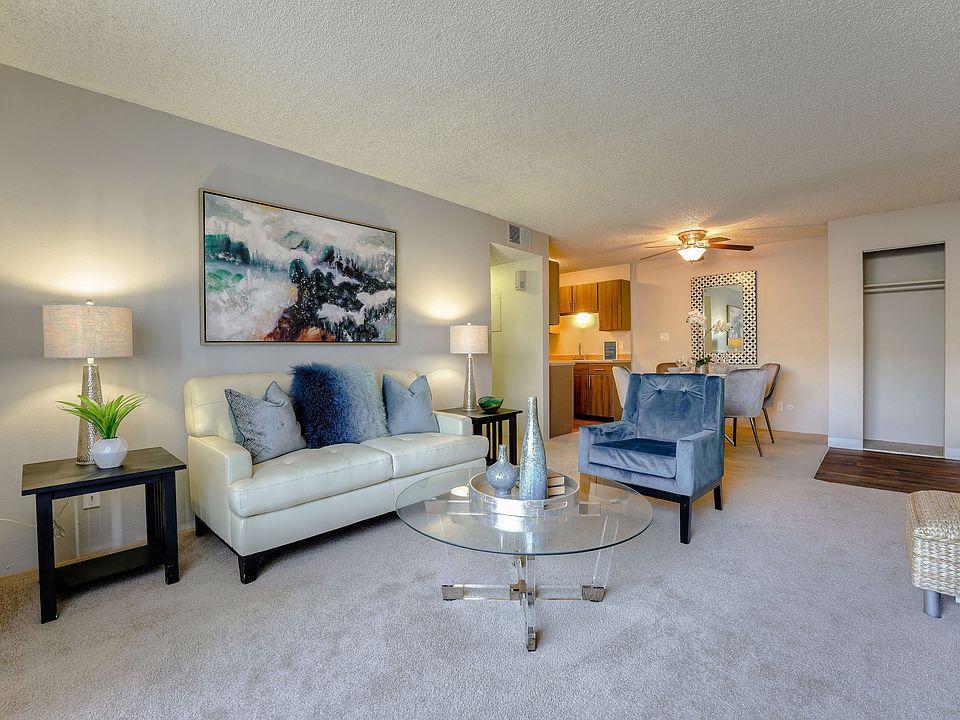 Model apartment living area with plush carpeting, a couch, and a view of the dining area.
