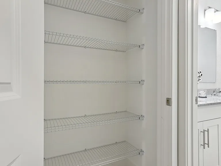 Pristine apartment showcasing a spacious white closet with elegant wire shelving adjacent to a modern bathroom with granite countertops.