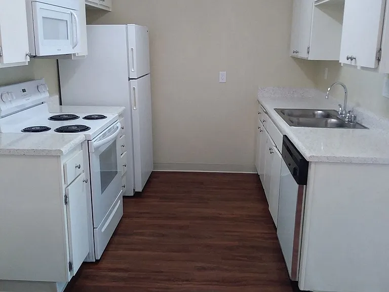 Kitchen with dark hardwood flooring and white kitchen appliances and cabinets at Teton Pines Apartments in Escondido, California.