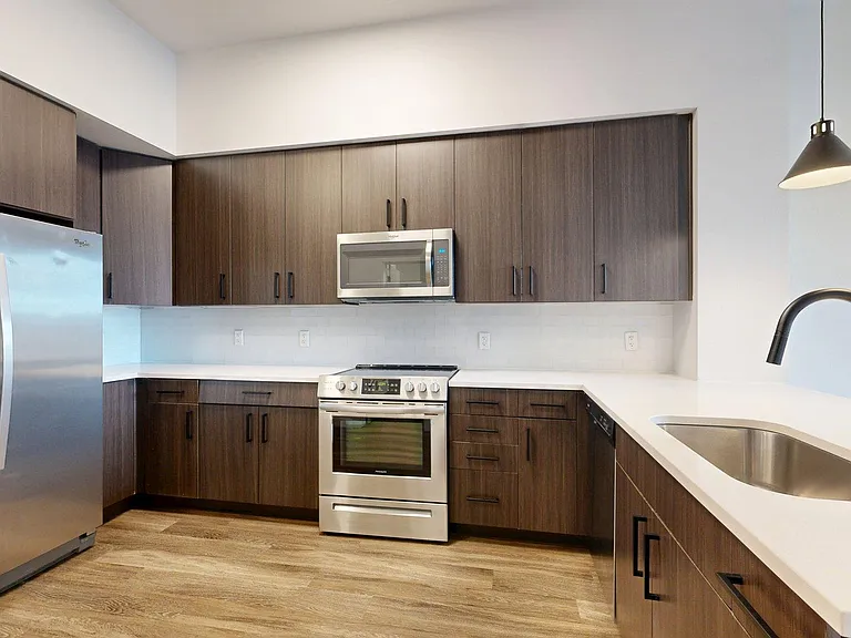 Apartment Kitchen with Stainless Steel Appliances, White Quartz Countertops and Plank Flooring.