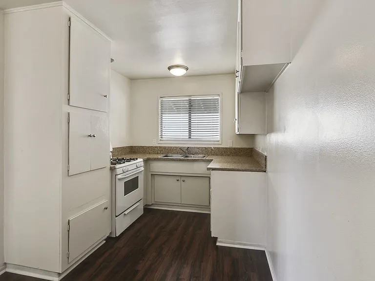 Kitchen with white gas range, granite countertops, white cabinets, and wood-inspired floors