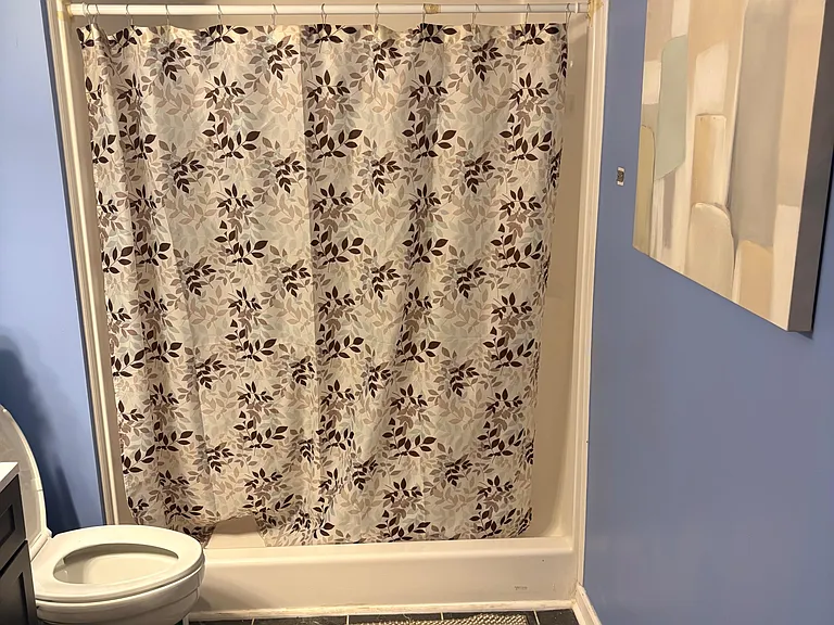 Bathroom with a tub/shower combo, patterned shower curtain, and tile flooring for easy upkeep.