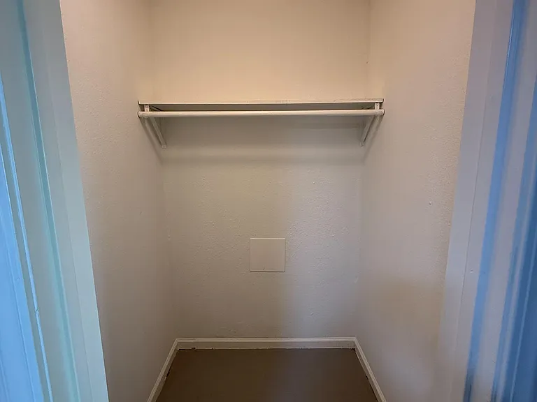 Walk-in storage closet with a hanging rod and upper shelf for organizing clothing, shoes, and seasonal items.