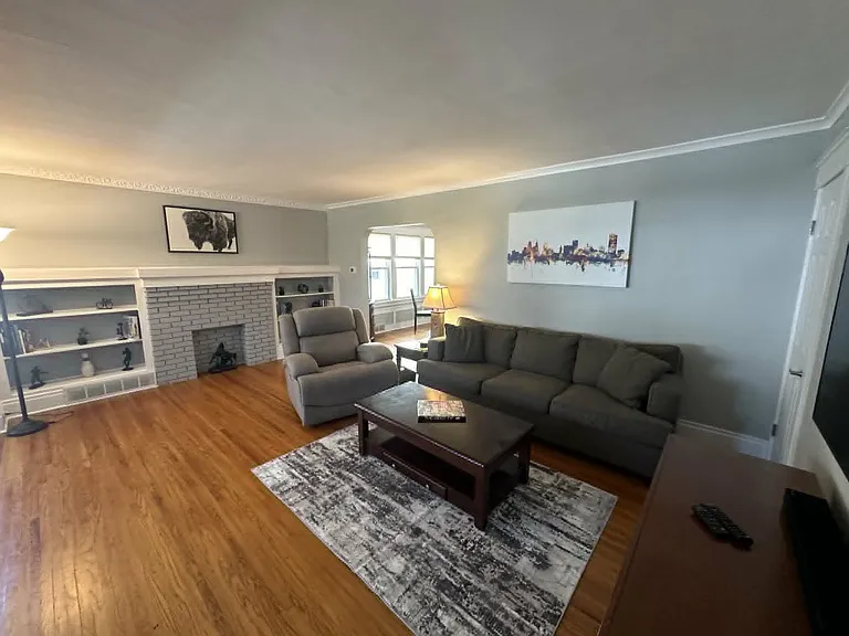 Another view of the inviting living room with decorative fireplace, built-in shelving, and abundant natural light.