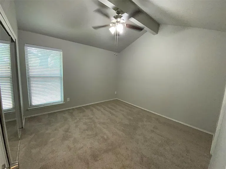 Vaulted ceiling room featuring light-toned carpeting, a window with horizontal blinds, and a ceiling fan with integrated lighting