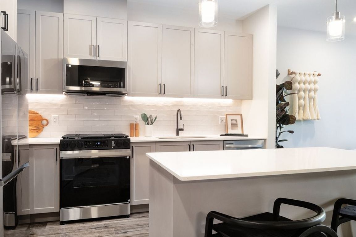 Modern kitchen with grey cabinetry, white tile backsplash, white quartz countertops, stainless steel appliances, and pendant lighting