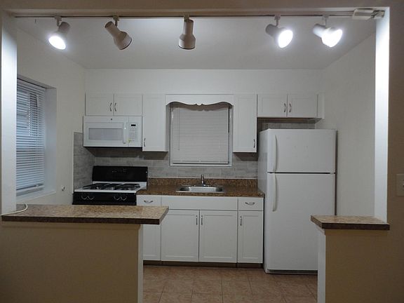 Working kitchen with gas stove, new microwave and full refrigerator, modern track lighting.