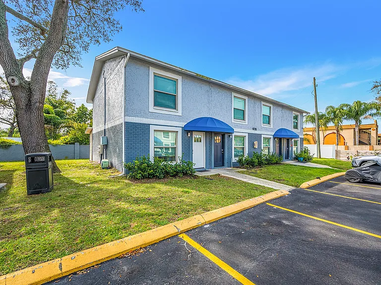 Charming duplex with blue awnings, manicured lawns, and ample parking nestled in a serene neighborhood.