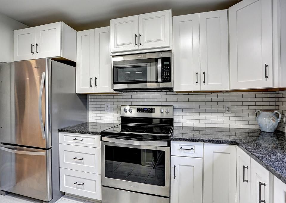 Bright white kitchen with granite countertop & stainless steel appliances.