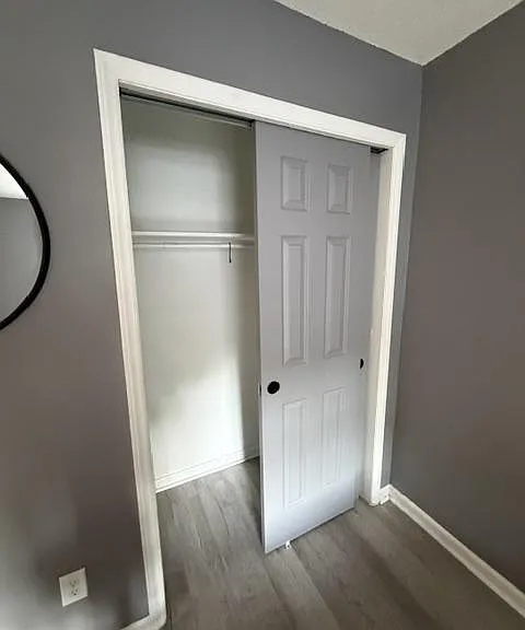 Private room with durable wood-look flooring and a reach-in closet with hanging rod and shelf for convenient storage.