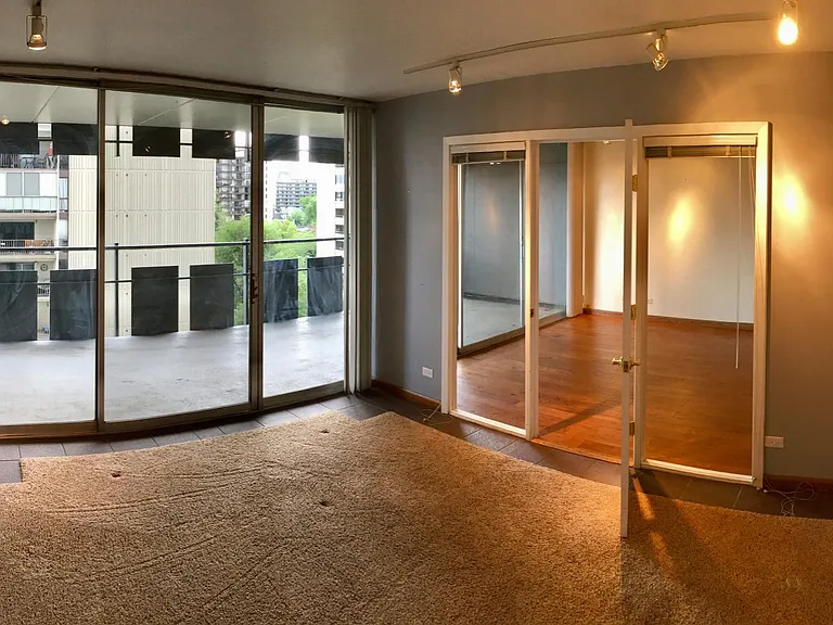 Bedroom looking through open door and windows to living room. Balcony has sliding glass doors in bedroom and living room.