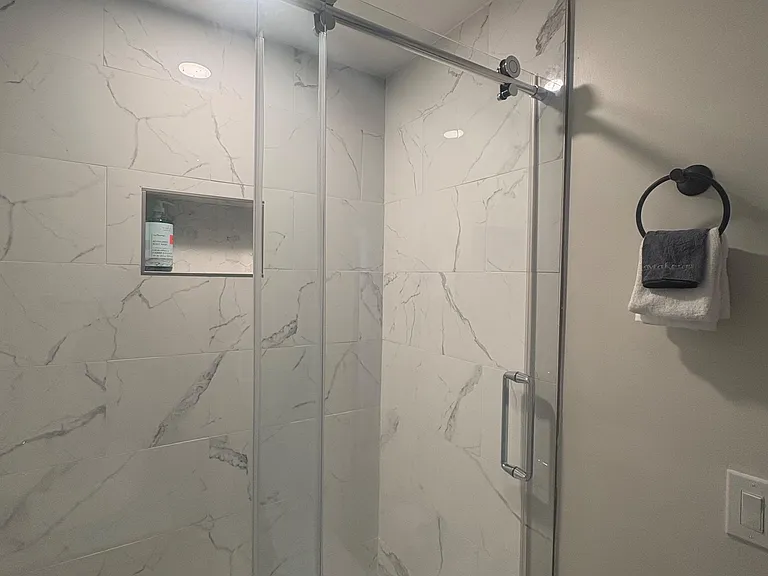 Walk-in shower with sliding glass enclosure, built-in niche shelving, and marble-look tile surround for easy maintenance.