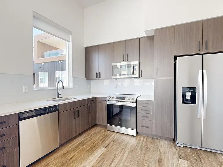 Apartment kitchen with stainless steel appliances, quartz countertops, and wood-style flooring.