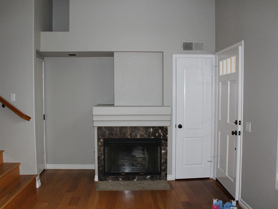 Living Room with fireplace and plantation shutters; front door on right, closet straight ahead, door to attached garage on left, stairs to up dining room and kitchen