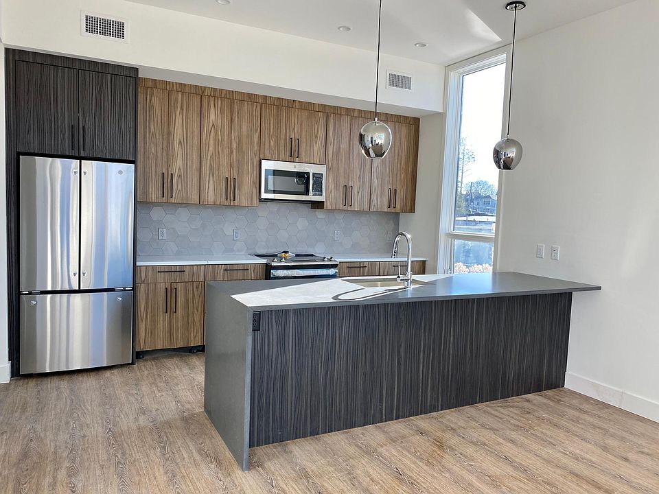 Modern two-tone kitchen cabinetry with quartz waterfall countertop & bar seating and stainless steel appliances.